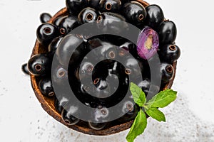 Black ripe Syzygium cumini fruits. Dark black java plum in a wood bowl at isolated white background. Green mint leaf on top of