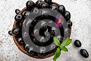 Black ripe Syzygium cumini fruits. Dark black java plum in a wood bowl at isolated white background. Green mint leaf on top of