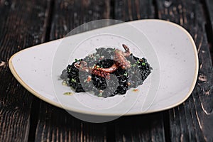 Black risotto with cuttlefish ink and octopus tentacles on irregular shape plate