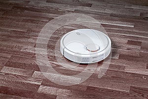 Black robotic vacuum cleaner runs on laminate and on tile floor. Robot controlled by voice commands for direct cleaning. Modern