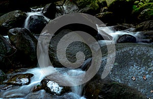 Black rock at waterfall with green moss and sunshine on rock. Waterfall is flowing in jungle. Waterfall in tropical forest. Nature