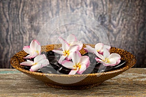 Black rocks and plumeria flwers on an old wood background