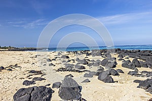 Black rocks scattered on the sandy beach of Griffiths Island of Port Fairy in Victoria, Australia.