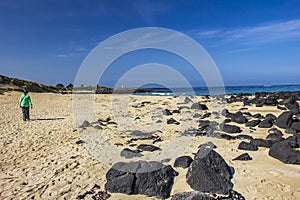 Black rocks scattered on the sandy beach of Griffiths Island of Port Fairy in Victoria, Australia.