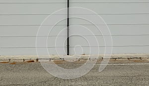 Black roof gutter on striped gray plaster wall. Worn concrete sidwalk and street in front. photo