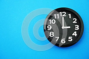 Black round clock showing five o`clock on blue background