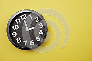 Black round clock showing three o`clock on yellow background