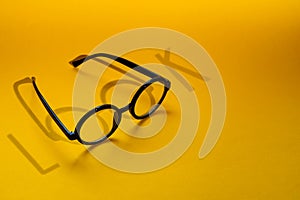 Black round glasses on a yellow background with hard shadow and the inscription look