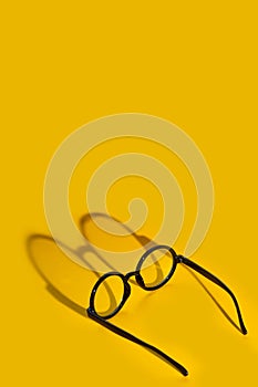 Black round glasses on a yellow background with hard shadow and the inscription look