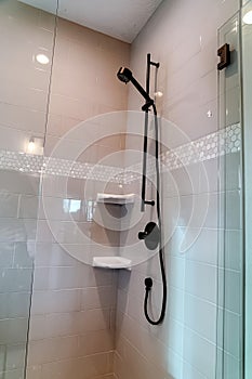Black round shower head on tile wall of shower stall with hinged glass door