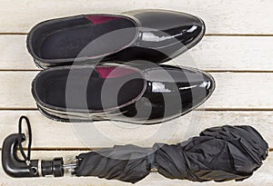 Black rubber galoshes with umbrella on wooden table