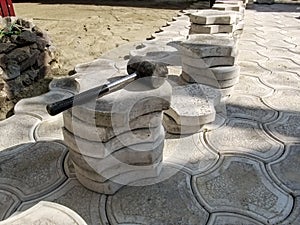 Black rubber mallet lies on top of a pile of gray figured paving slabs among unfinished work on the paving tiles in patio. Concept