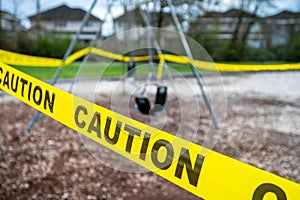 Black rubber swings in closed public playground surrounded by yellow caution tape during Corvid-19 Coronavirus pandemic