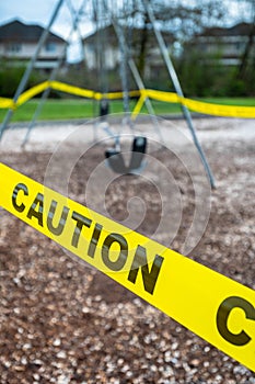 Black rubber swings in closed public playground surrounded by yellow caution tape during Corvid-19 Coronavirus pandemic