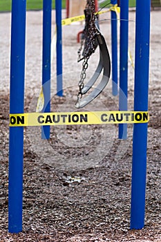 Black rubber swings in closed public playground surrounded by yellow caution tape during Corvid-19 Coronavirus pandemic