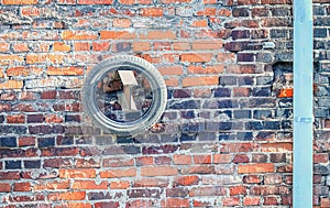 Black rubber tire hanging on wooden detail of red brick wall building with stailess steel water pipe on a side on sunny day photo