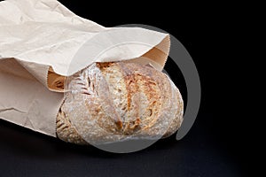 Black rye bread in flour and kraft paper bag on black background