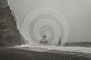 Black sand beach Reynisfjara, Iceland during foggy weather, mountain range with sea and beach in front
