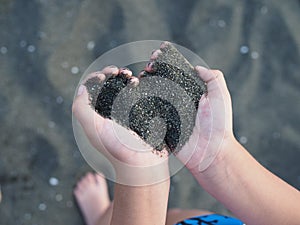 Black sand in children`s hands in the form of a heart