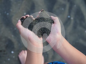 Black sand in children`s hands in the form of a heart