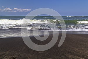 Black sand volcanic beach and white waves of ocean in Bali, Indonesia