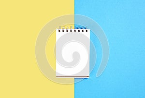 Black screen notebook blank and pen placed on pastel yellow and blue background.