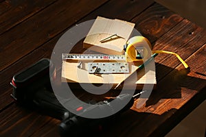 The black screw and is measured by a yellow tape measure with a ruler on a wooden board background. The concept of tools