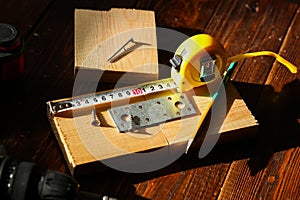 The black screw and is measured by a yellow tape measure with a ruler on a wooden board background. The concept of tools