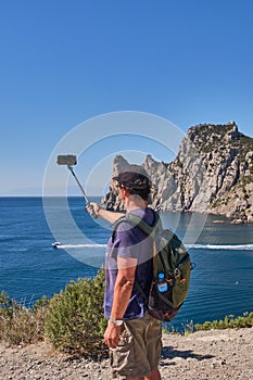 Black Sea coast, Crimea. An Asian elderly man takes photos over the background of the Blue Bay on the tourist route Golitsyn trail