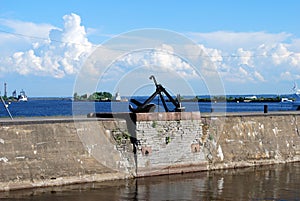 A black Sea ship anchor with a chain lies in the port on a granite slab.