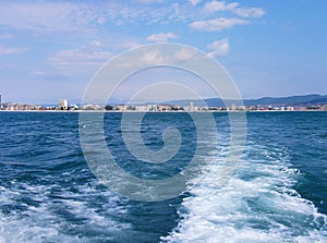 Black sea surface summer wave background. View from yacht. Exotic seascape with clouds and town on horizon. Sea nature tranquility