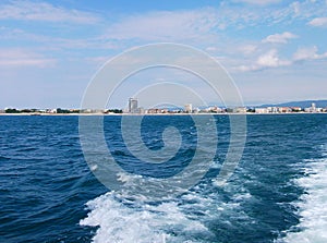 Black sea surface summer wave background. View from yacht. Exotic seascape with clouds and town on horizon. Sea nature tranquility