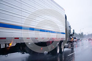 Black semi truck with reefer trailer on raining highway
