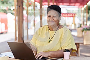 Black senior woman using laptop at outdoor cafe and looking at camera smiling