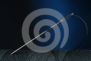 Black sewing thread with needle on dark blue background, closeup