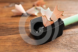 Black sharpener with pencil shavings on wooden table, closeup. Space for text