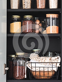 Black shelf in the kitchen with various cereals and seeds in glass jars
