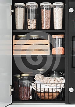 Black shelf in the kitchen with various cereals and seeds in glass jars