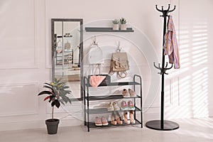 Black shelving unit with shoes and different accessories near white wall in hall. Storage idea