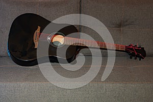 black shiny acoustic guitar with red strings, mahagony fretboard and picks lying on gray couch