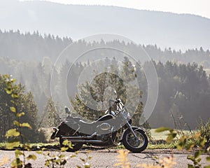 Black shiny high-speed motorcycle parked on empty narrow country roadside on sunny summer day.