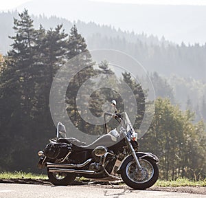 Black shiny high-speed motorcycle parked on empty narrow country roadside on sunny summer day.