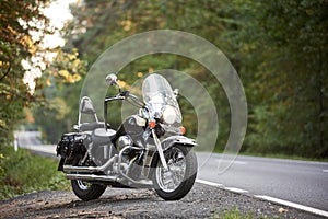 Black shiny high-speed motorcycle parked on empty narrow country roadside on sunny summer day.