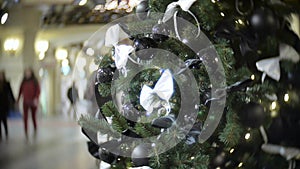 Black shiny and matte balls and white bow. New Year`s and abstract blurred shopping mall background with Christmas tree