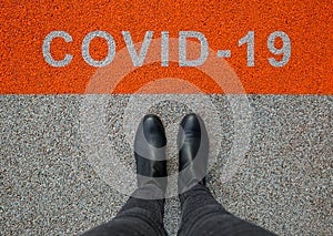 Black shoes standing on the asphalt concrete floor with orange line. Feet shoes walking in outdoor. Coronavirus in the world.