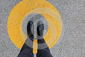 Black shoes standing in yellow circle on the asphalt concrete floor. Comfort zone or frame concept. Feet standing inside comfort