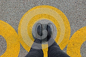 Black shoes standing in yellow circle on the asphalt concrete floor. Comfort zone or frame concept. Feet standing inside comfort