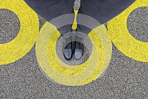 Black shoes standing in yellow circle on the asphalt concrete floor. Comfort zone or frame concept. Feet standing inside comfort