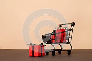 Black shopping cart with paper bags and red gift boxes on beige background,copy space. black friday concept