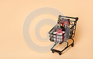 Black shopping cart with paper bags and small gift boxes on beige background,copy space. black Friday concept